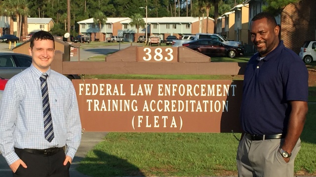 Ben Reynolds and James Mays stand by the sign to the Federal Law Enforcement Training Accreditation (FLETA)