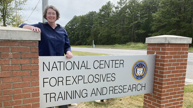 Program Manager Christiana Halsey stands with the entry sign for the National Center for Explosives Training and Research