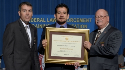 FLETA Board Chair Brian Peters (left) and FLETA Executive Director Gary Mitchell, Ph.D. present the accreditation certificate to the USMS Training Division